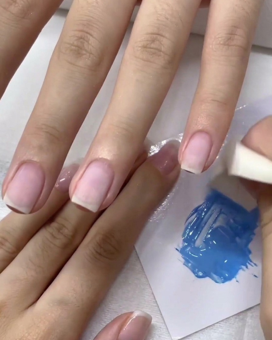 A makeup sponge dabbing blue gel onto a fingernail to create an ombre effect.