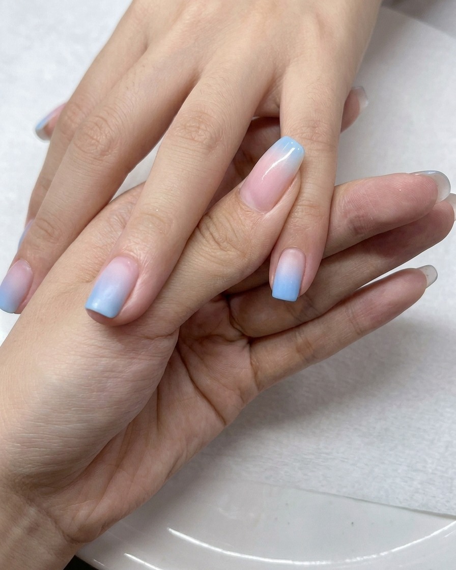 A brush applying a layer of clear gel top coat over the ombre gradient nails.