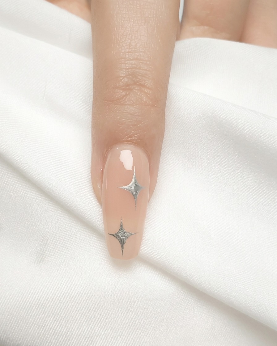 A nail brush applying a sheer coat of nude gel polish to a natural nail.