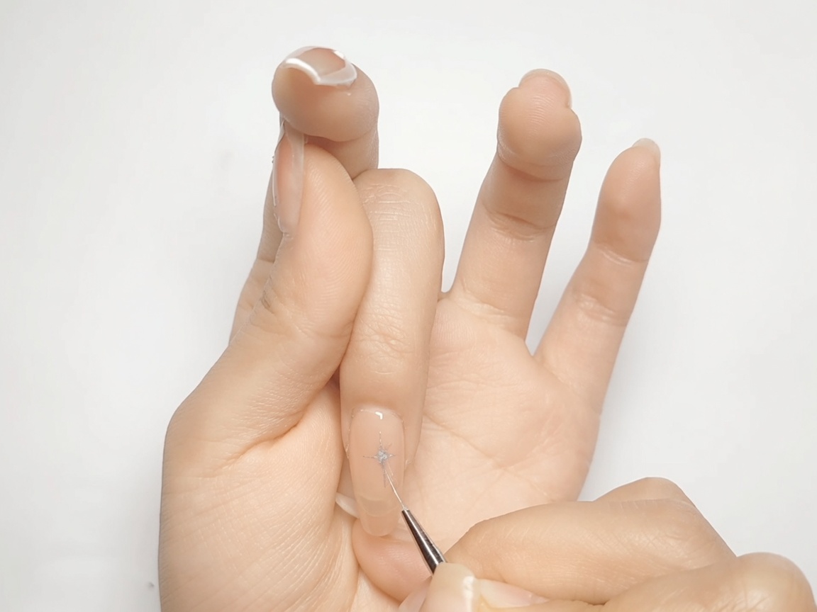 A nail art brush filling in the diamond-shaped corners of a metallic silver star on a nude nail.