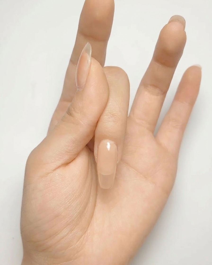A close-up of a nude gel nail with a metallic silver cross shape painted on the surface.
