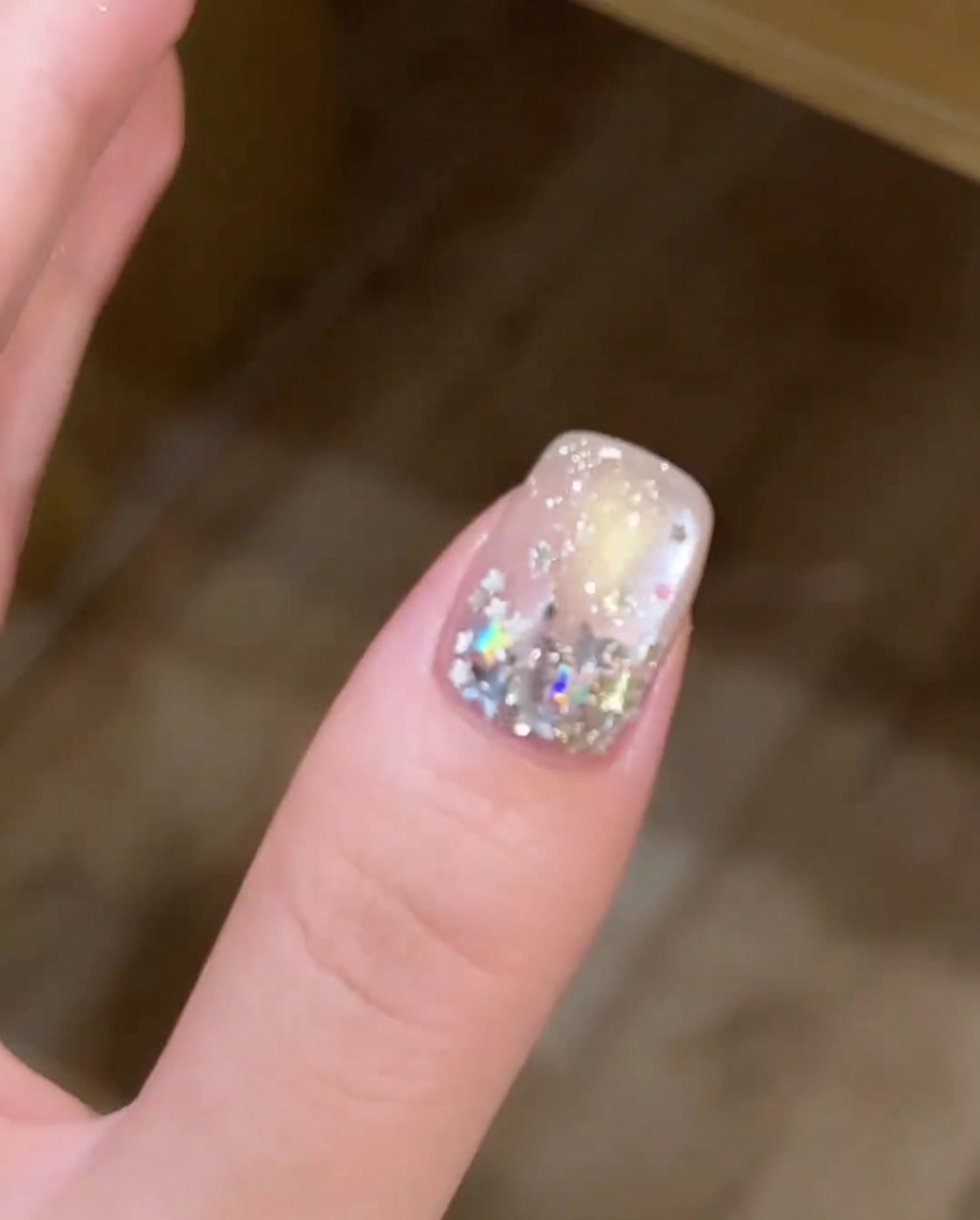 A close-up view of a brush applying a thin layer of white gel polish to the tip of a nail.