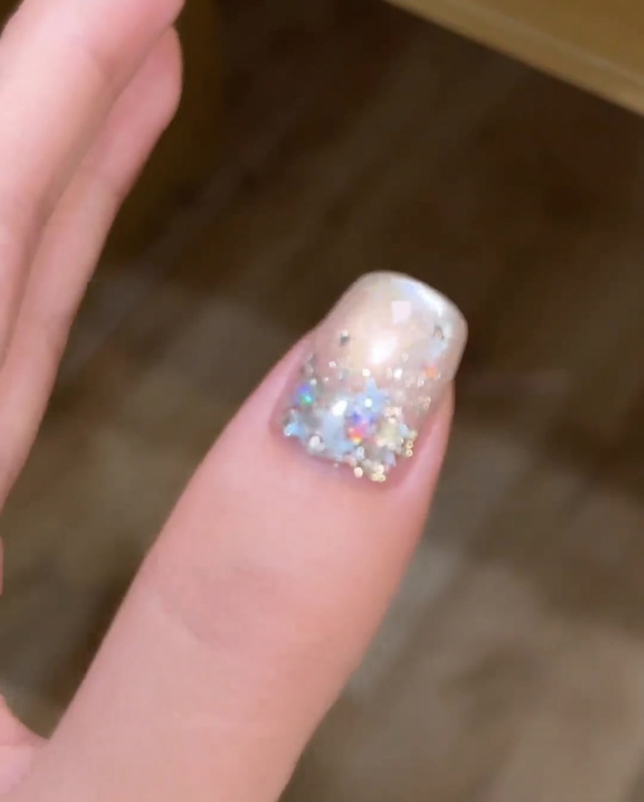 A brush applying a coat of silver metallic cat-eye gel polish over a white-painted nail.