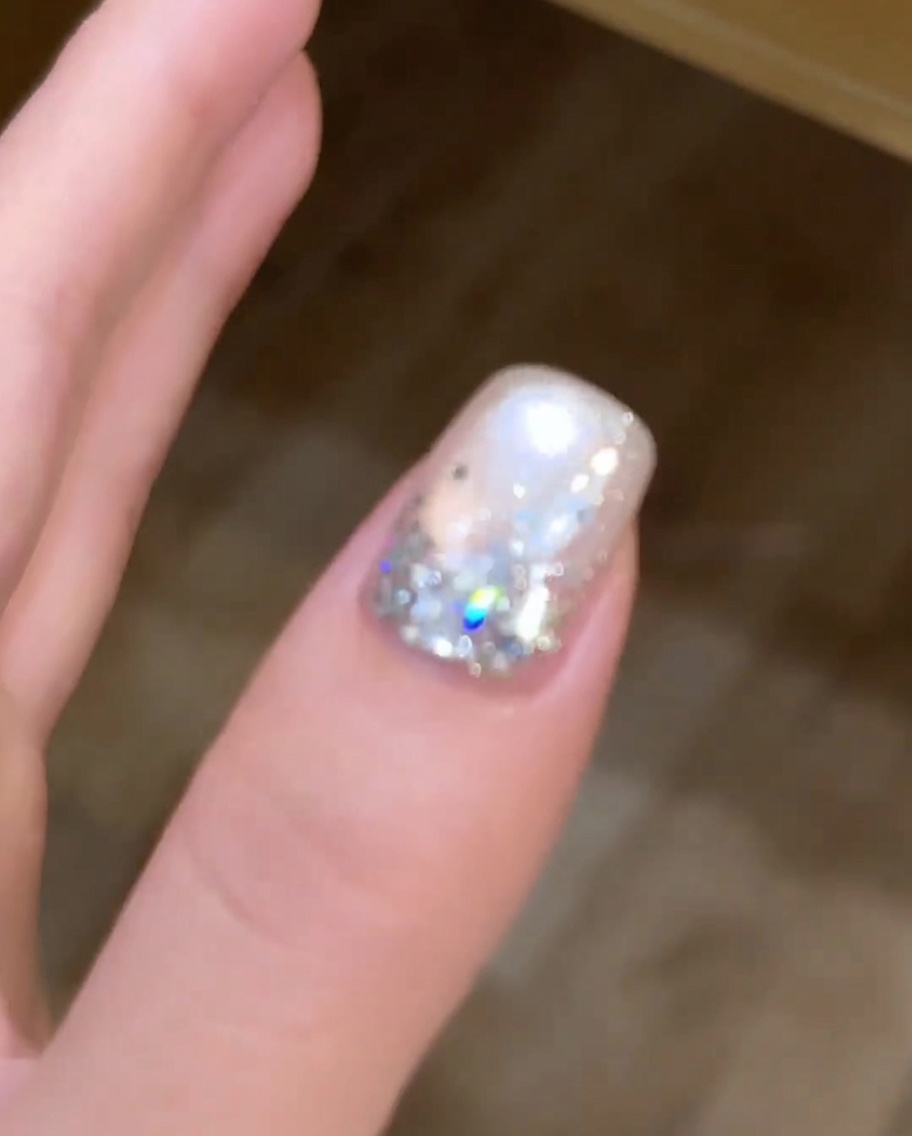 A magnet being held over a wet silver cat-eye gel nail to manipulate the metallic pigments into a circular pattern.