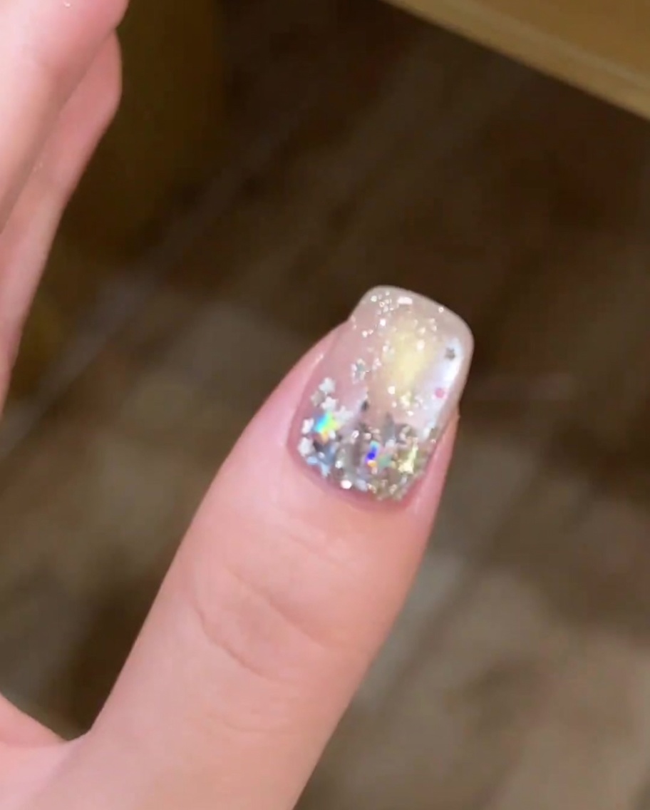 A nail with a mix of large and small star-shaped sequins being arranged on the nail plate.