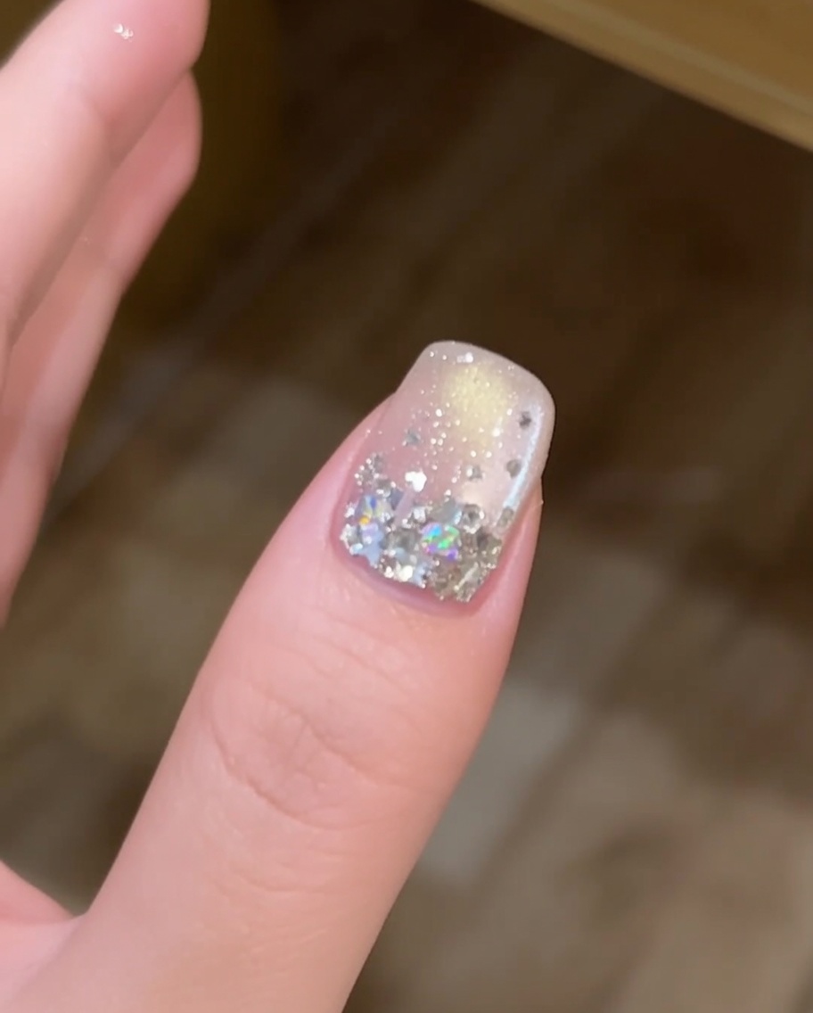 A thin layer of clear builder gel being applied with a brush over a nail decorated with star sequins.