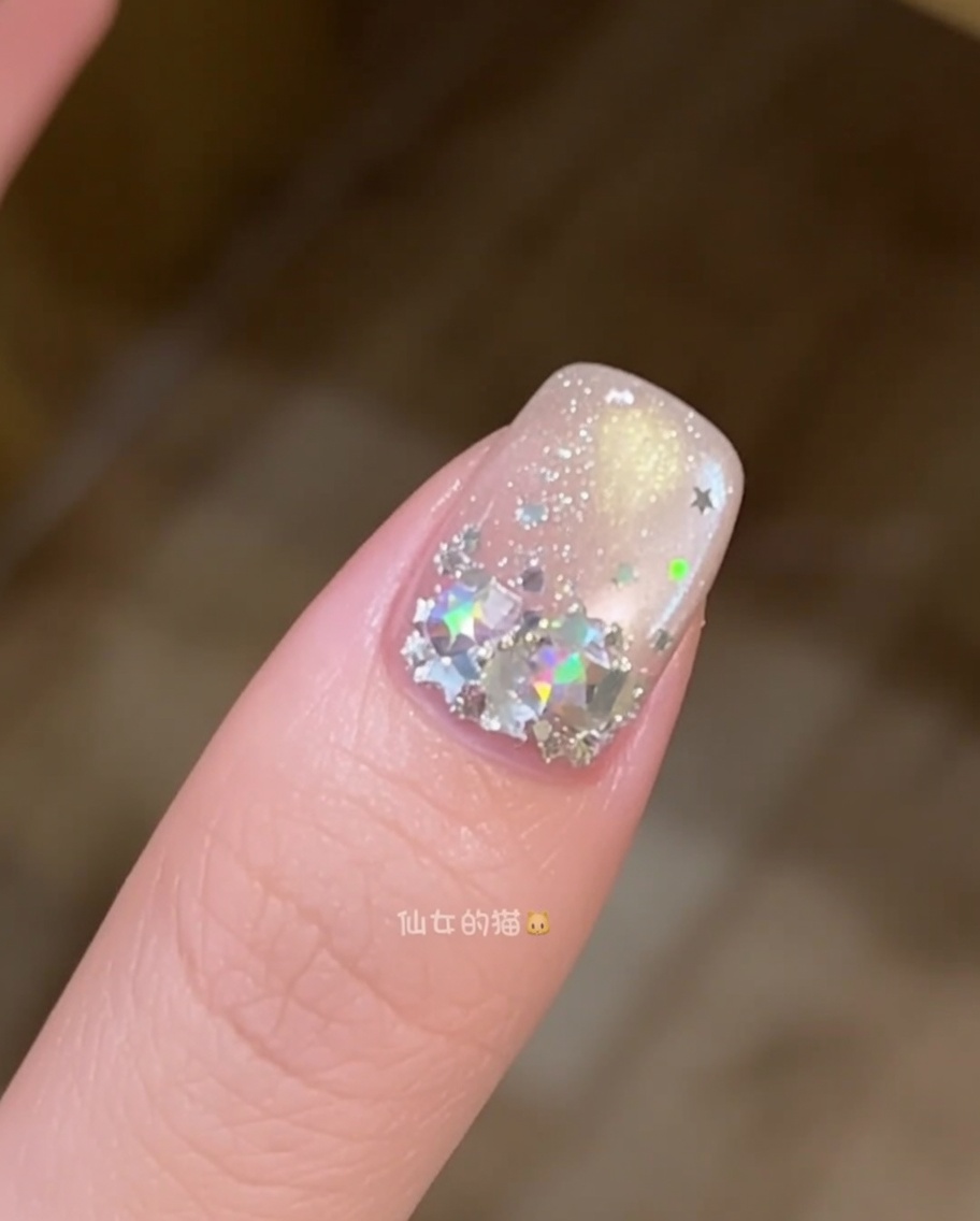 A close-up of a nail brush smoothing out a layer of clear builder gel on a nail decorated with star-shaped sequins.