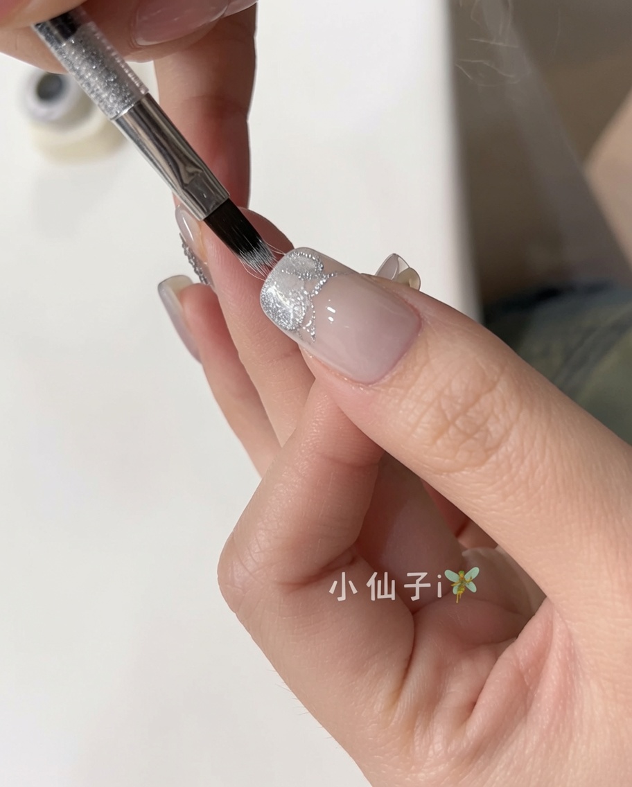 A brush applying a shimmering silver cat-eye gel polish onto a natural, prepped nail.