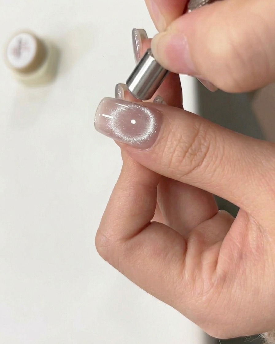 A magnetic tool being held in a circular motion over a wet cat-eye gel nail to create a ring effect.