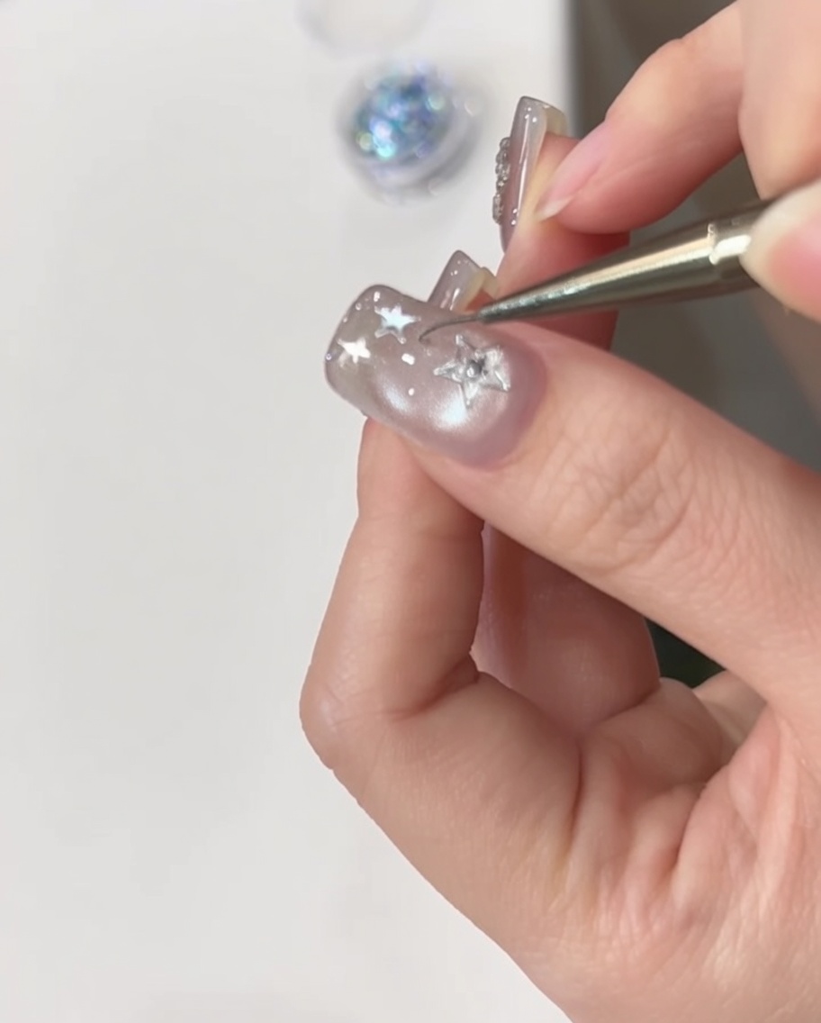 A hand positioned under a UV nail lamp curing the decorated nail.