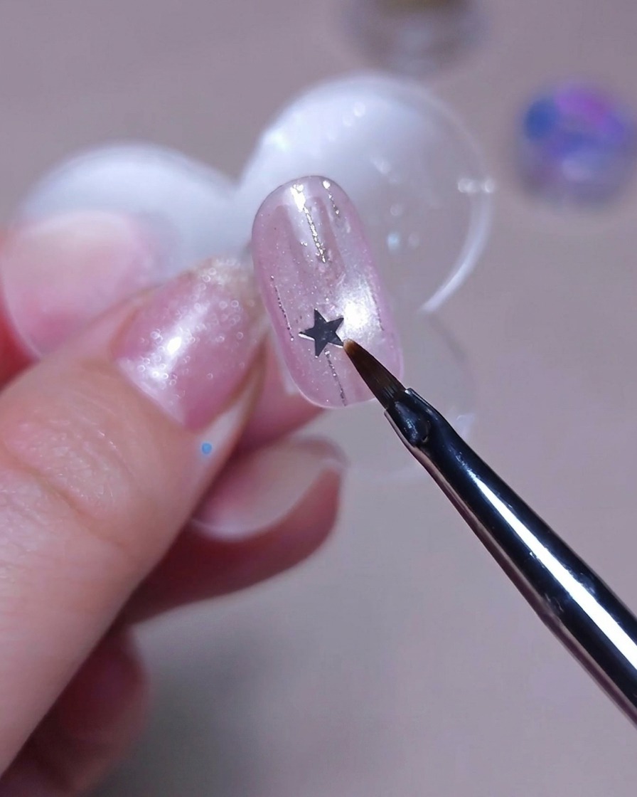 A fine brush placing a small silver star sequin onto a nail.