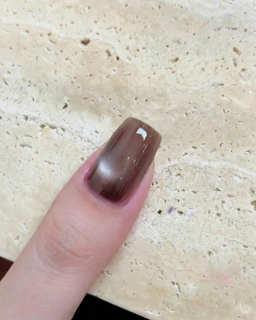 A close-up of a glossy brown nail featuring a circular, reflective cat-eye effect after curing.