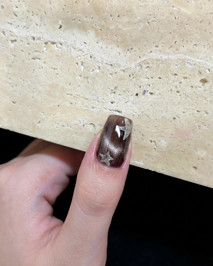 A brown cat-eye nail decorated with two hand-painted platinum silver stars.