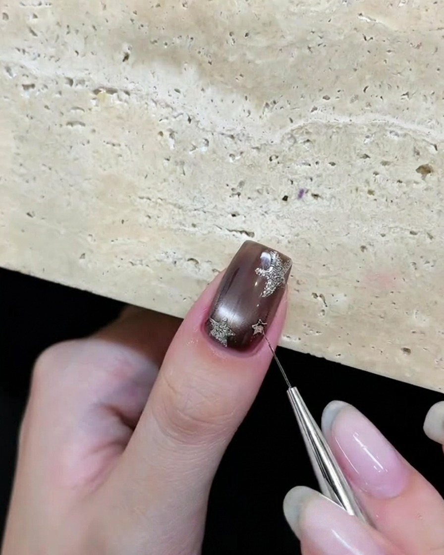 A tool placing silver star glitter pieces onto a brown gel nail.