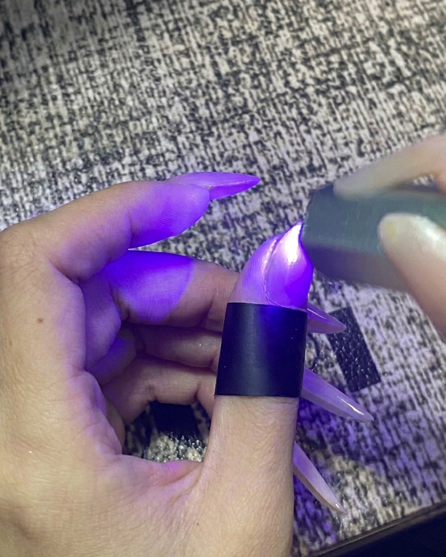 A finger placed inside a portable UV/LED nail lamp with the light activated.