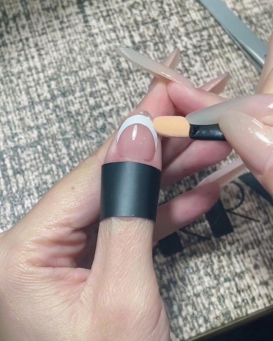 An eyeshadow applicator rubbing silver chrome powder onto the tip of a nail.