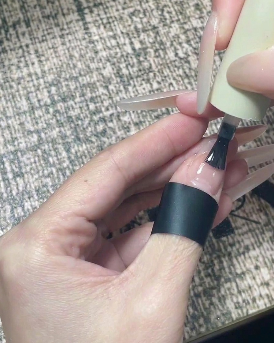 A brush applying clear glossy top coat to a finished nail design featuring black stars.