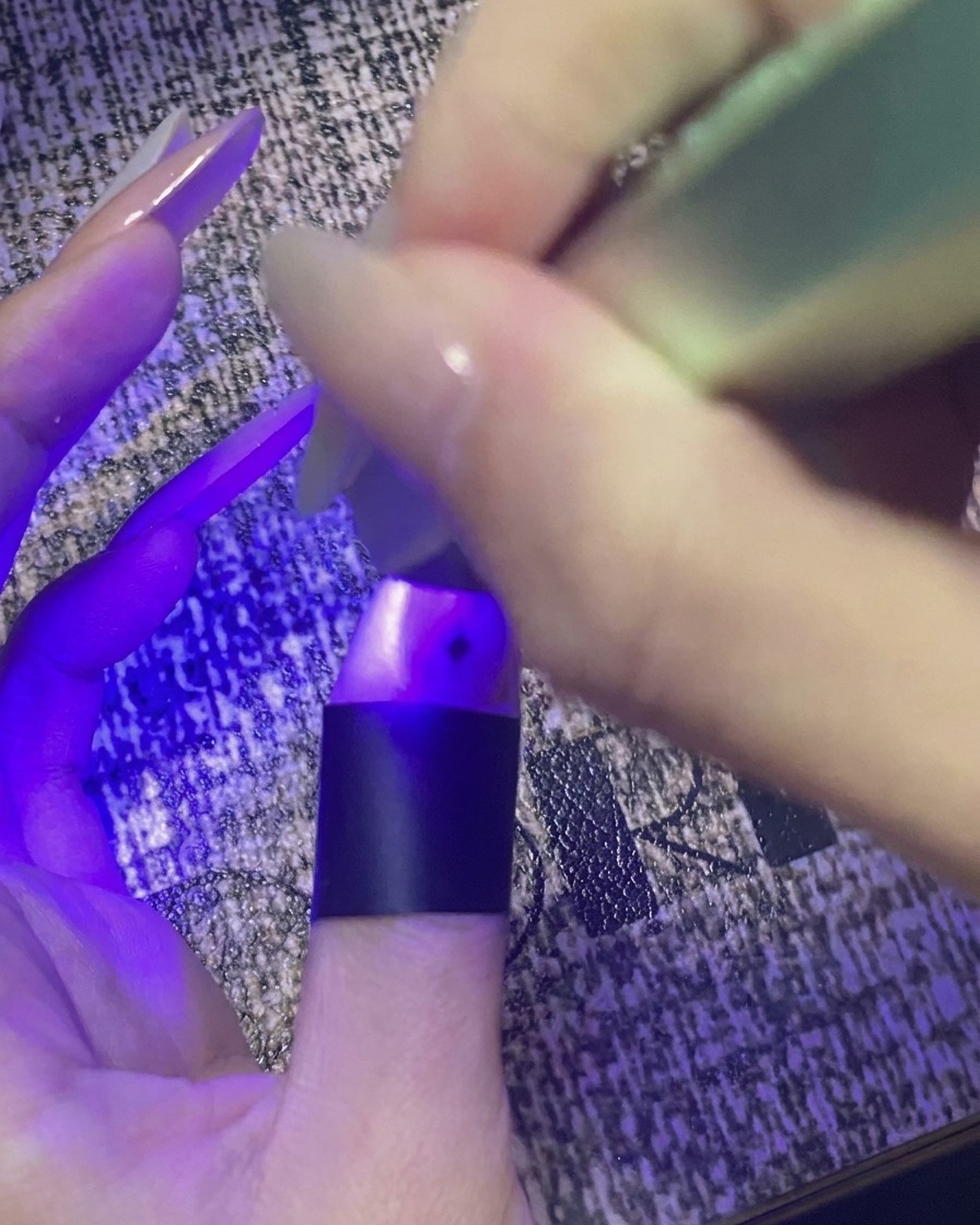 A thumb with star nail art curing under a purple mini UV/LED light.