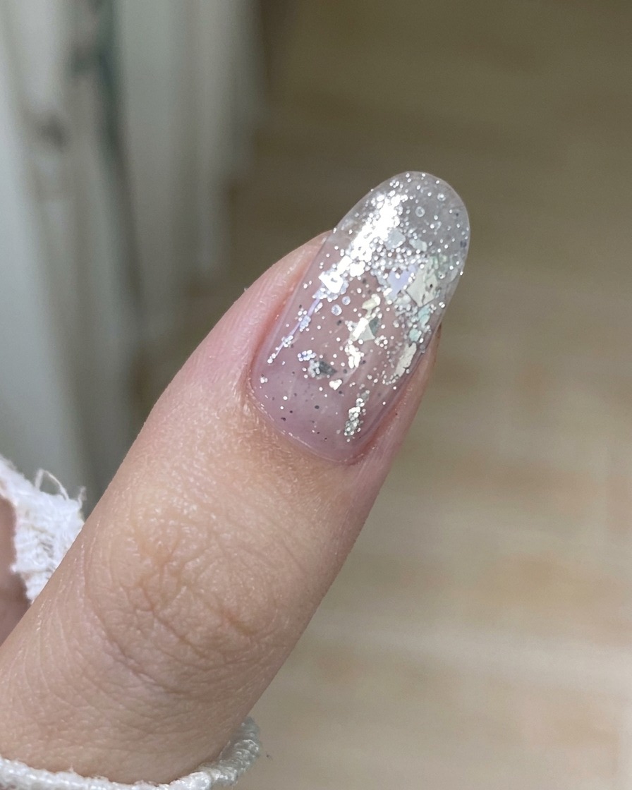 A close-up shot of a metal tool carefully lifting the edge of an old gel layer from a fingernail.