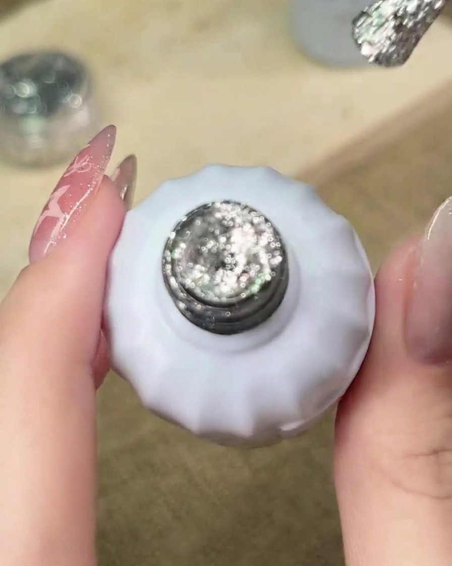 A brush applying silver glitter gel to the free edge of the nail, starting the gradient process.