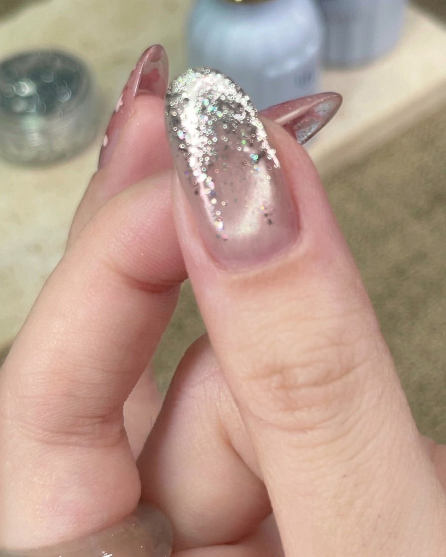 Close-up of a tool placing a small, metallic star sequin onto a silver glitter gradient nail.