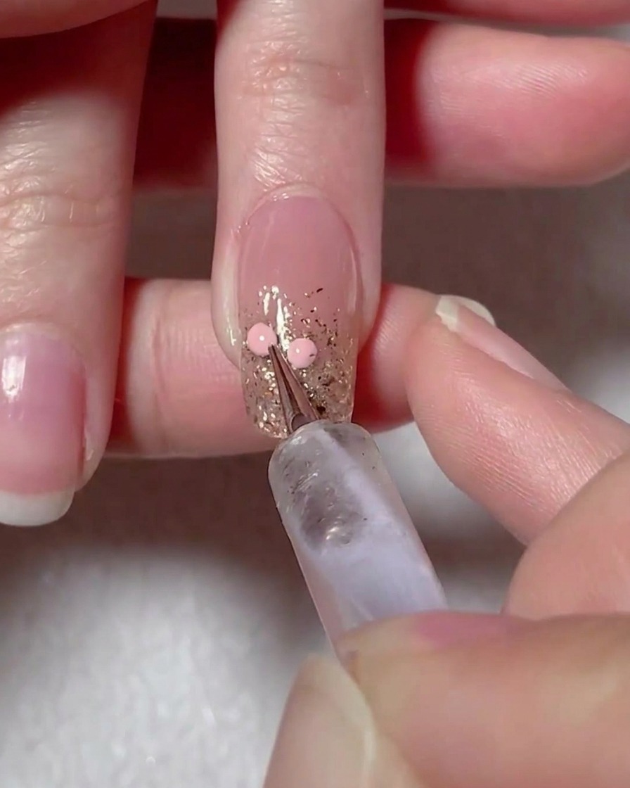 A dotting tool placing two pink gel dots on the nail surface to map out a heart design.