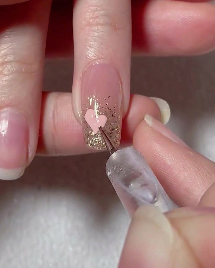 A liner brush connecting pink gel dots to form a heart shape on the nail.