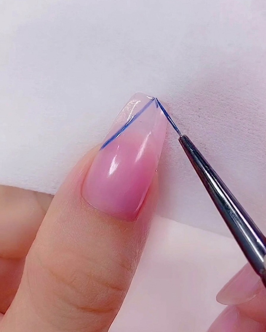 A close-up of a liner brush refining the edges of a blue heart design on the nail.