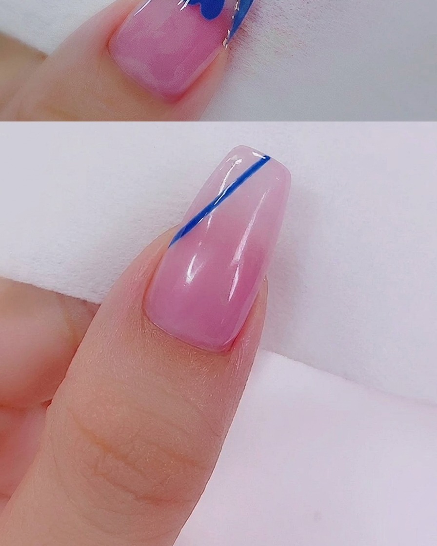 A close-up of a blue heart shape being filled in with blue gel using a fine nail art liner brush.