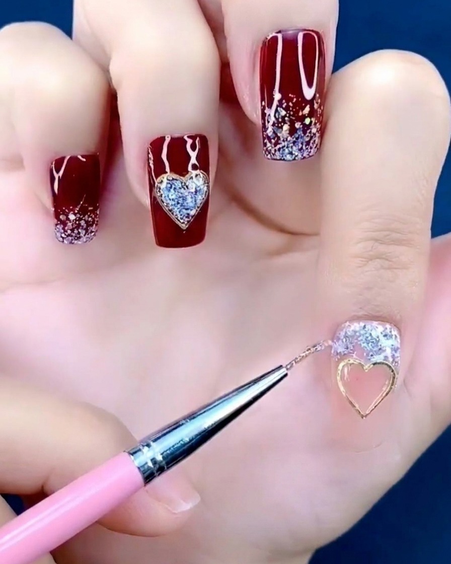 Tweezers holding a small metal heart charm and placing it onto the center of a fingernail.