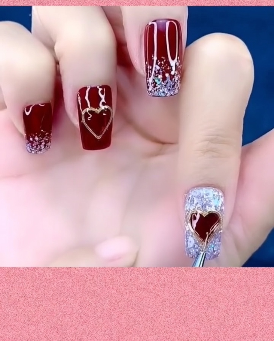 A nail art brush applying a top coat around the edges of a metal heart charm on a nail.