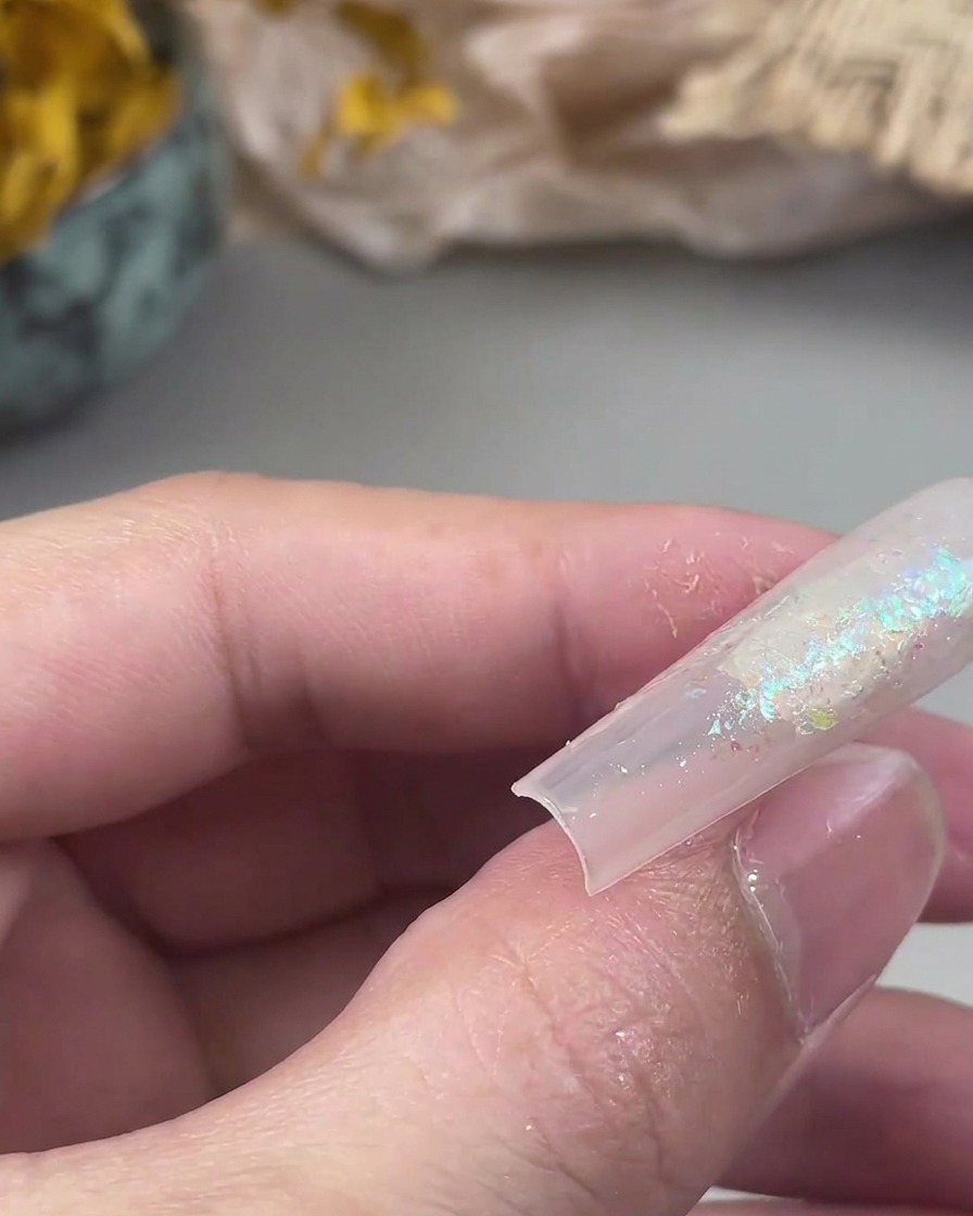 A small flat brush pressing loose glitter particles onto a tacky gel surface on a nail.