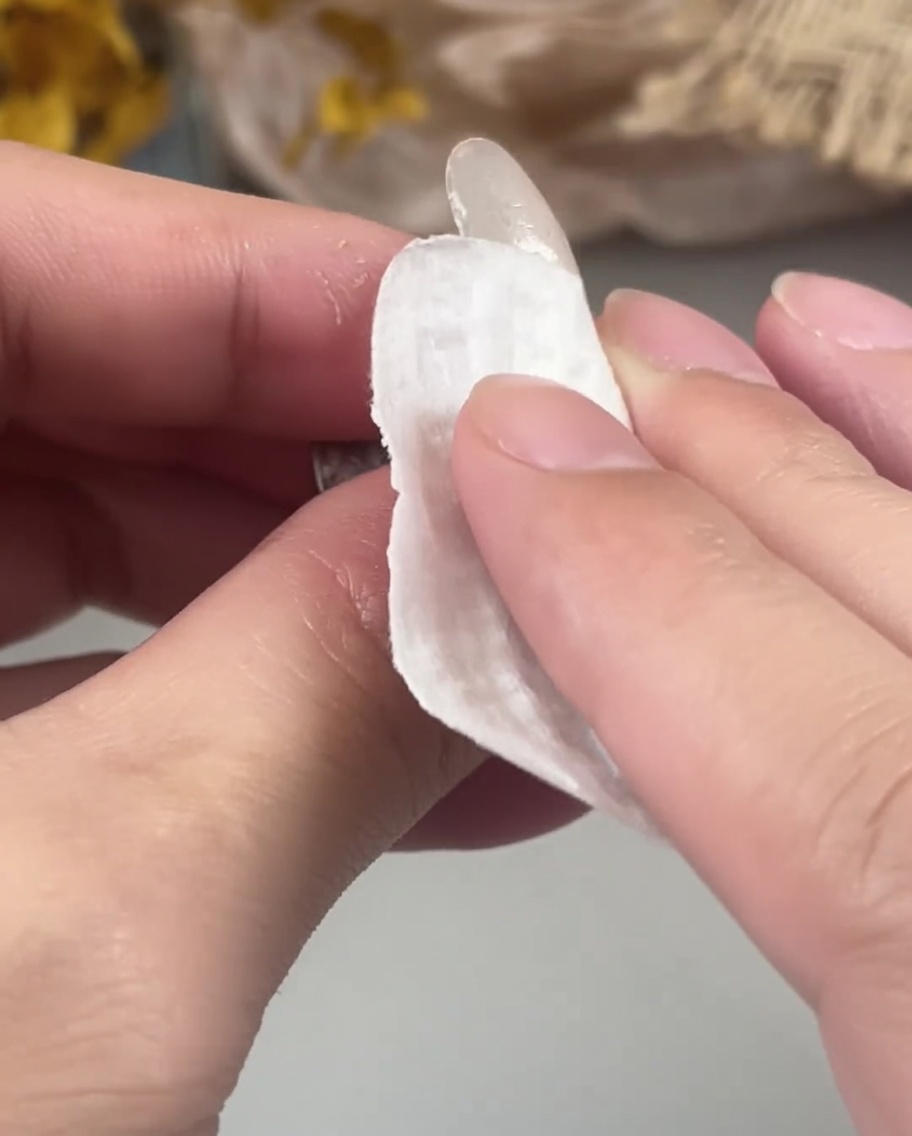 A hand using a lint-free wipe to clean the surface of a cured gel nail.