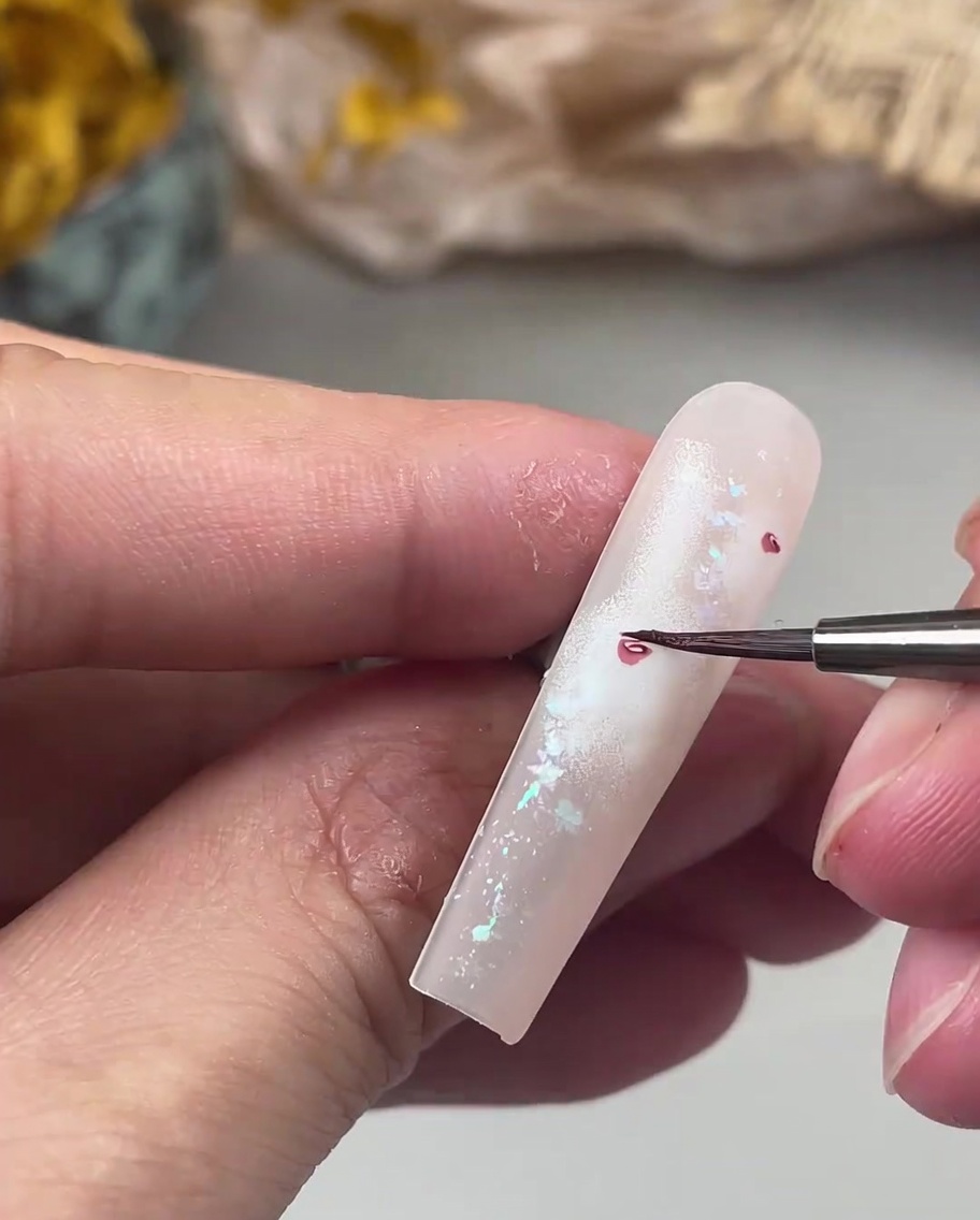 A fine-liner nail art brush painting delicate, small dark pink petals around a central rose heart on a nail.