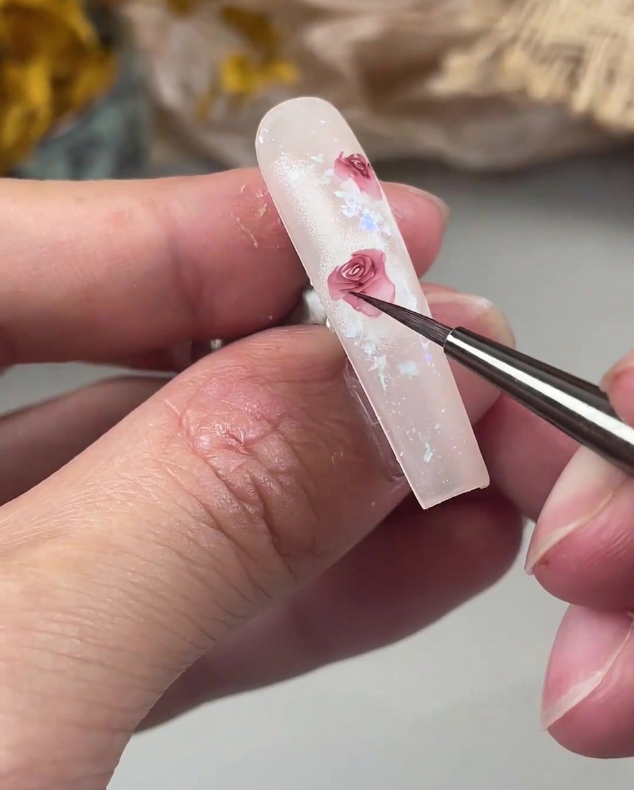 A detail brush adding delicate, outward-curving petals to the edge of a rose design on a nail.