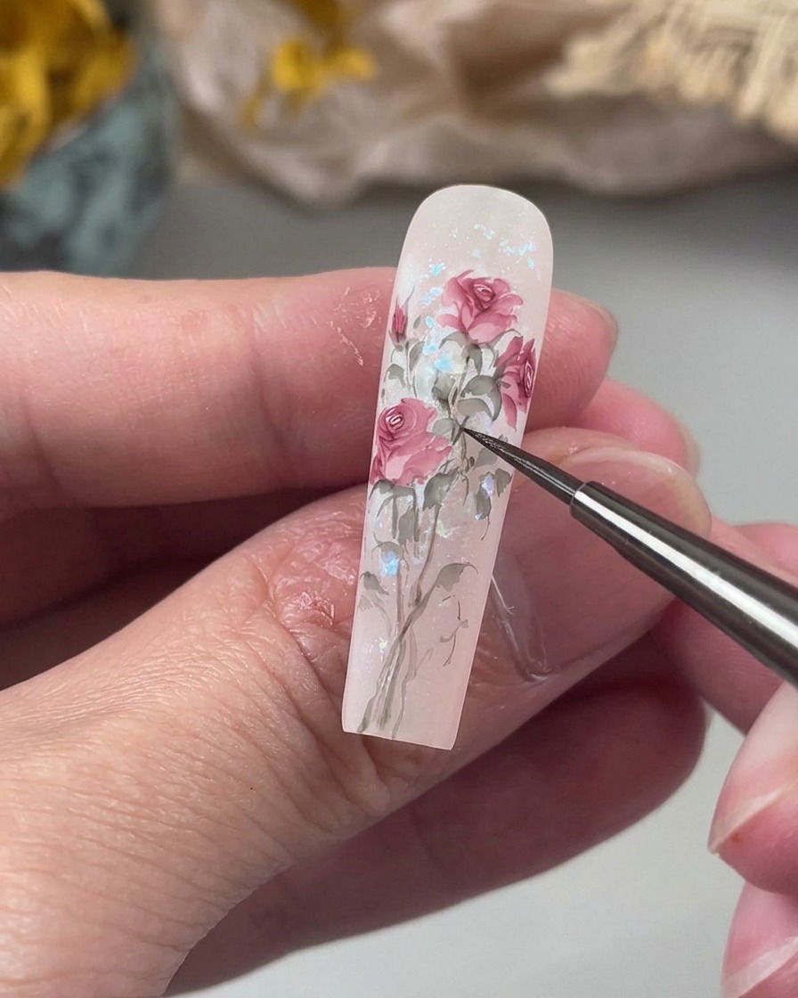 A fine detail brush drawing delicate, slightly curved stems in a soft green shade, connecting painted floral elements on the nail.