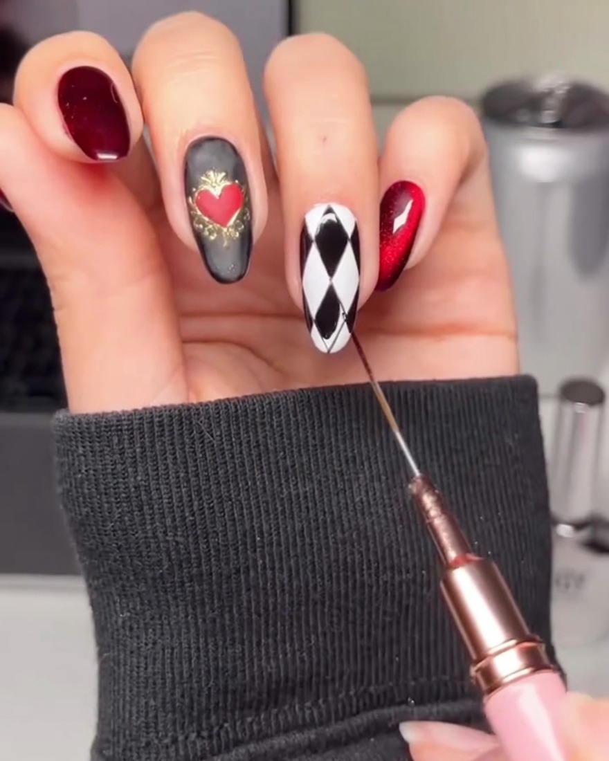 A hand using a liner brush to fill in alternating diamond shapes on a white nail with black gel.