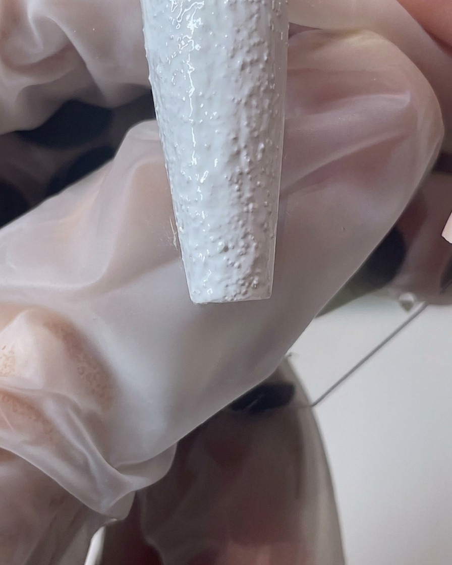 Close-up of a brush manipulating white sand gel to create a thicker, textured edge on the nail.