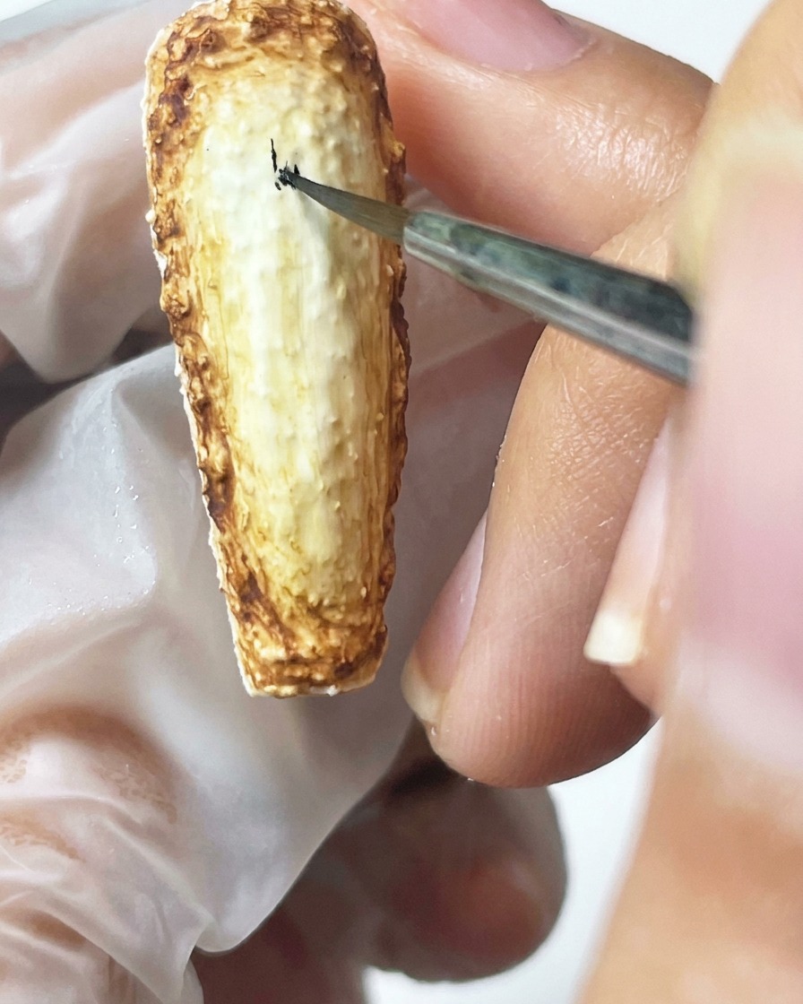 A fine liner brush carefully painting black text onto the textured, pigmented nail surface.