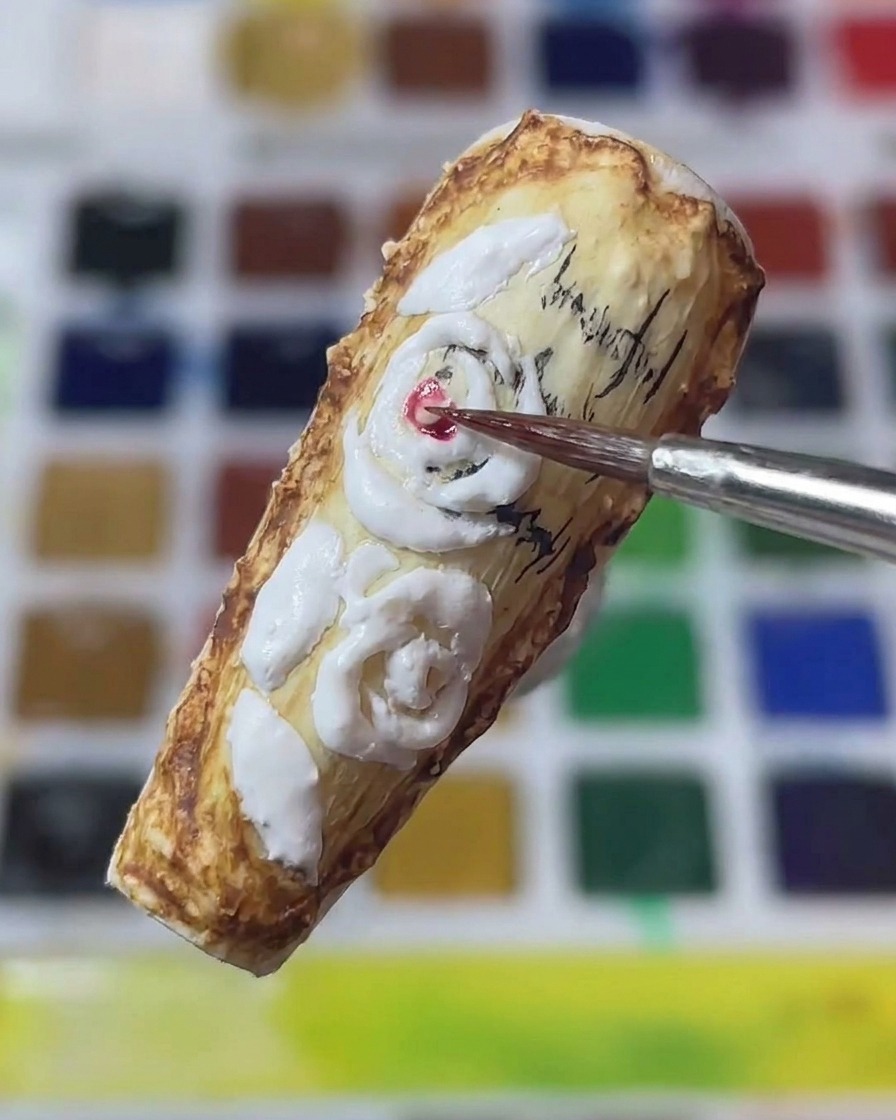 A close-up of a fine nail art brush applying red pigment to the center of white 3D sculpted roses on a vintage-style nail.