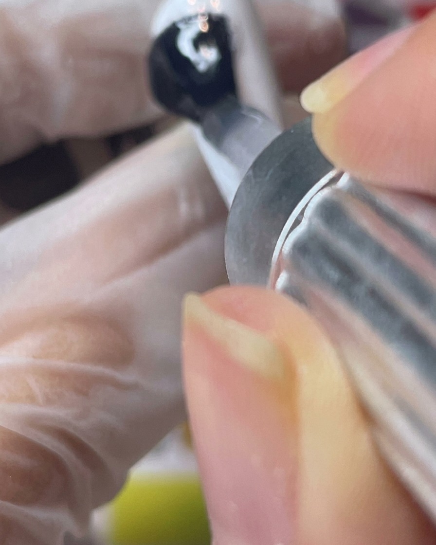 Applying a clear matte top coat over a white painted nail tip.