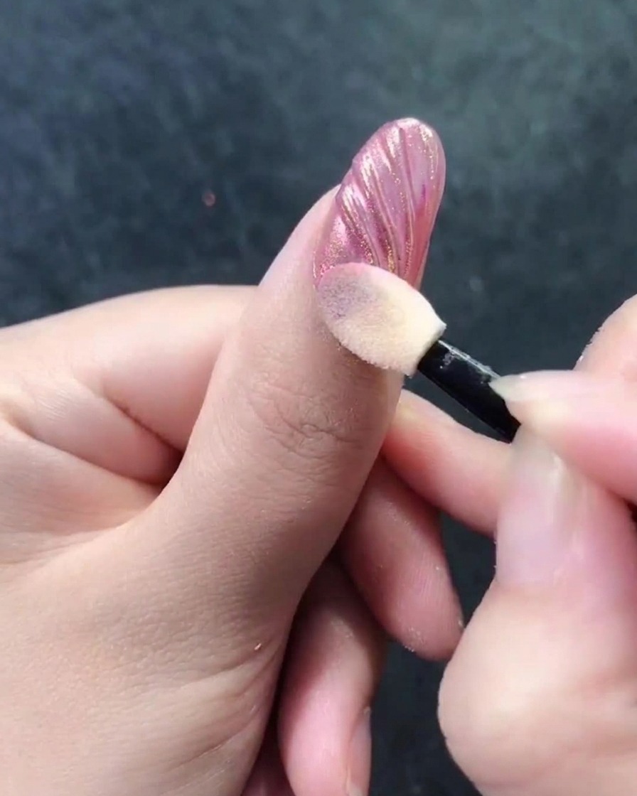 A sponge-tip applicator buffing chrome powder into the ridges of a seashell nail design.
