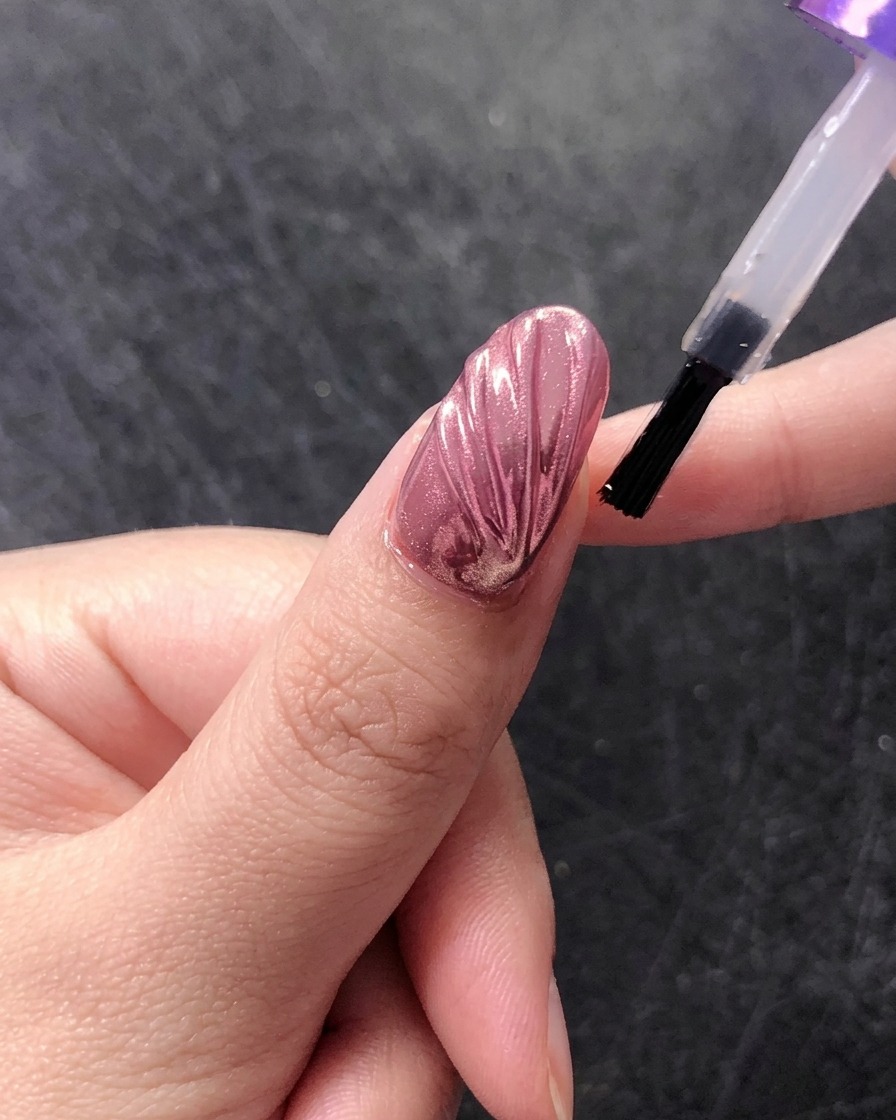 A brush applying a final glossy top coat over a chrome seashell nail design.