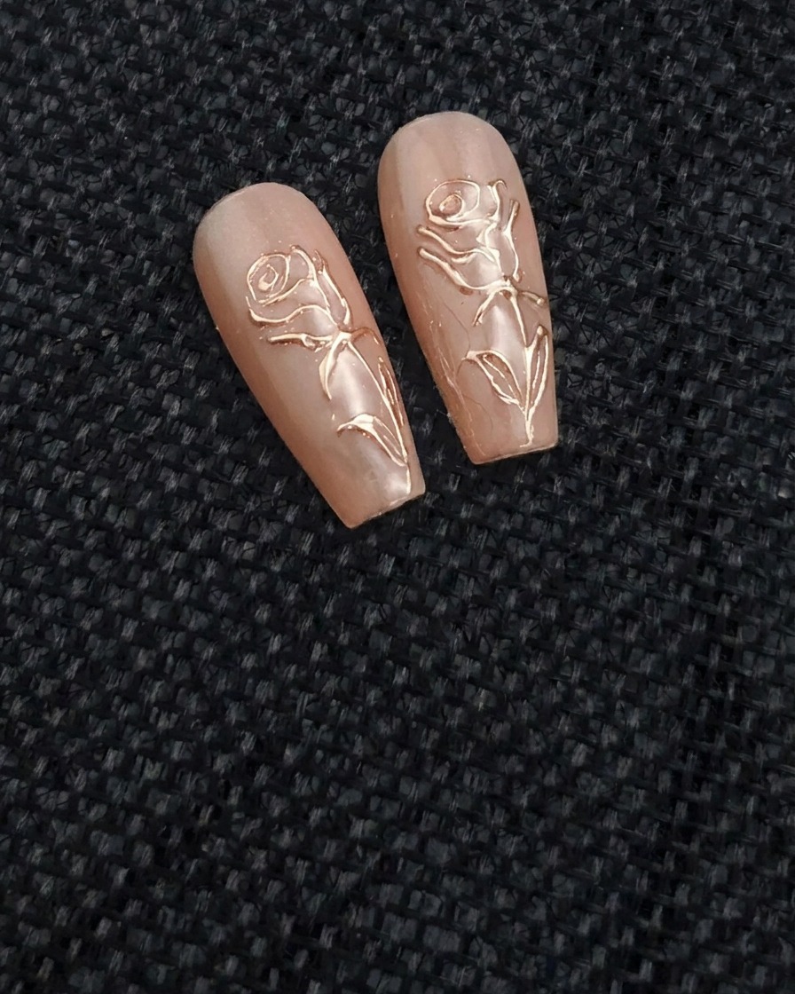 A thin nail art brush applying a clear, raised gel line in the shape of a rose on a nude-colored nail.