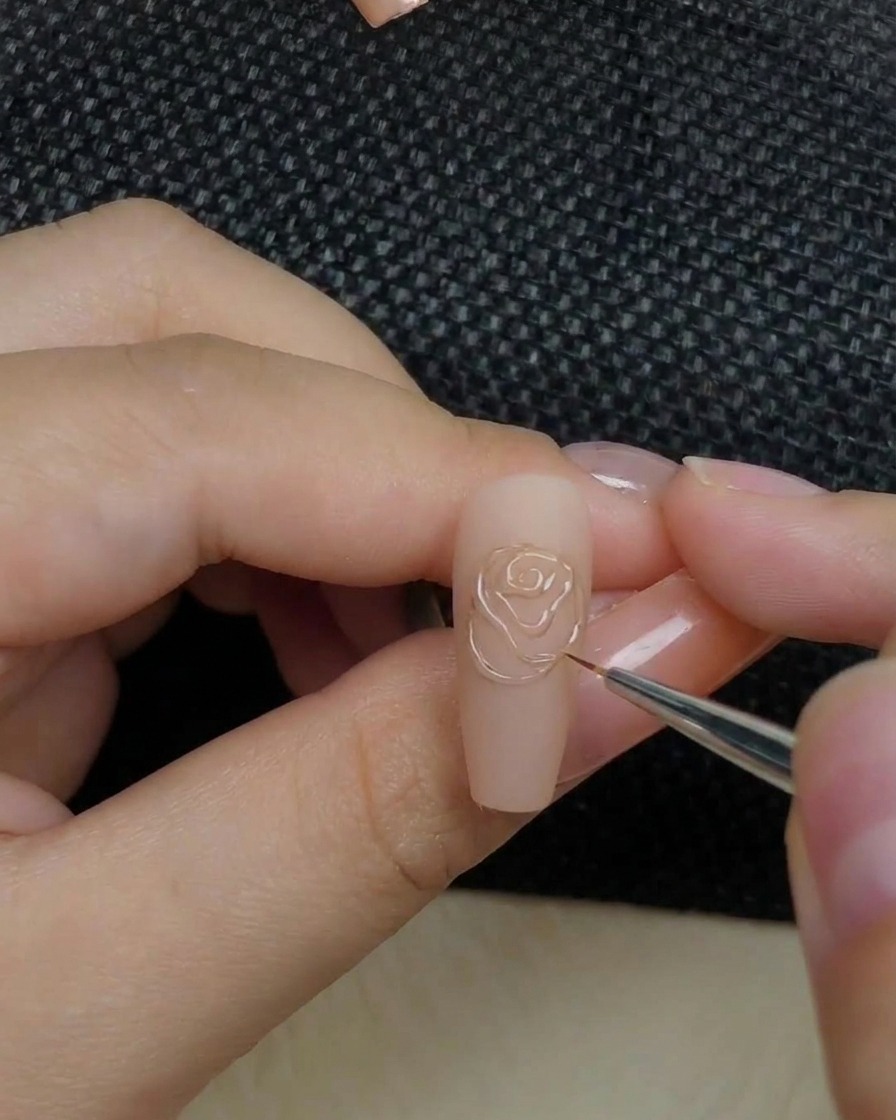 A close-up of a hand placing a nail with a raised rose design into a curing lamp.
