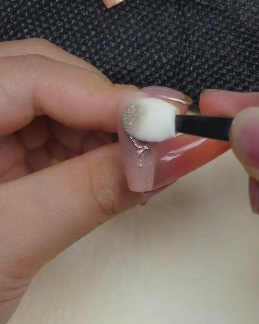 An eyeshadow-style applicator sponge pressing metallic chrome powder onto a raised rose design on a nail.