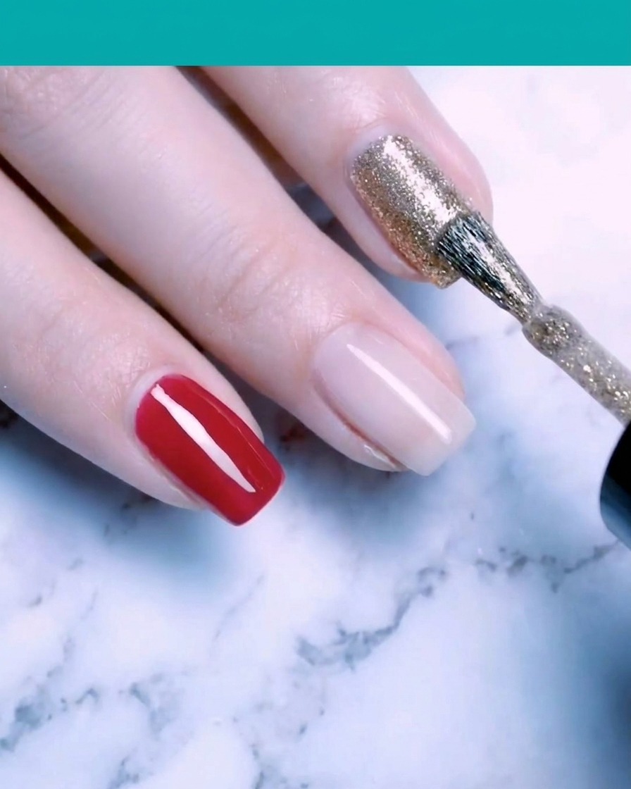 A nail brush applying sparkling fine gold glitter gel polish to a fingernail.