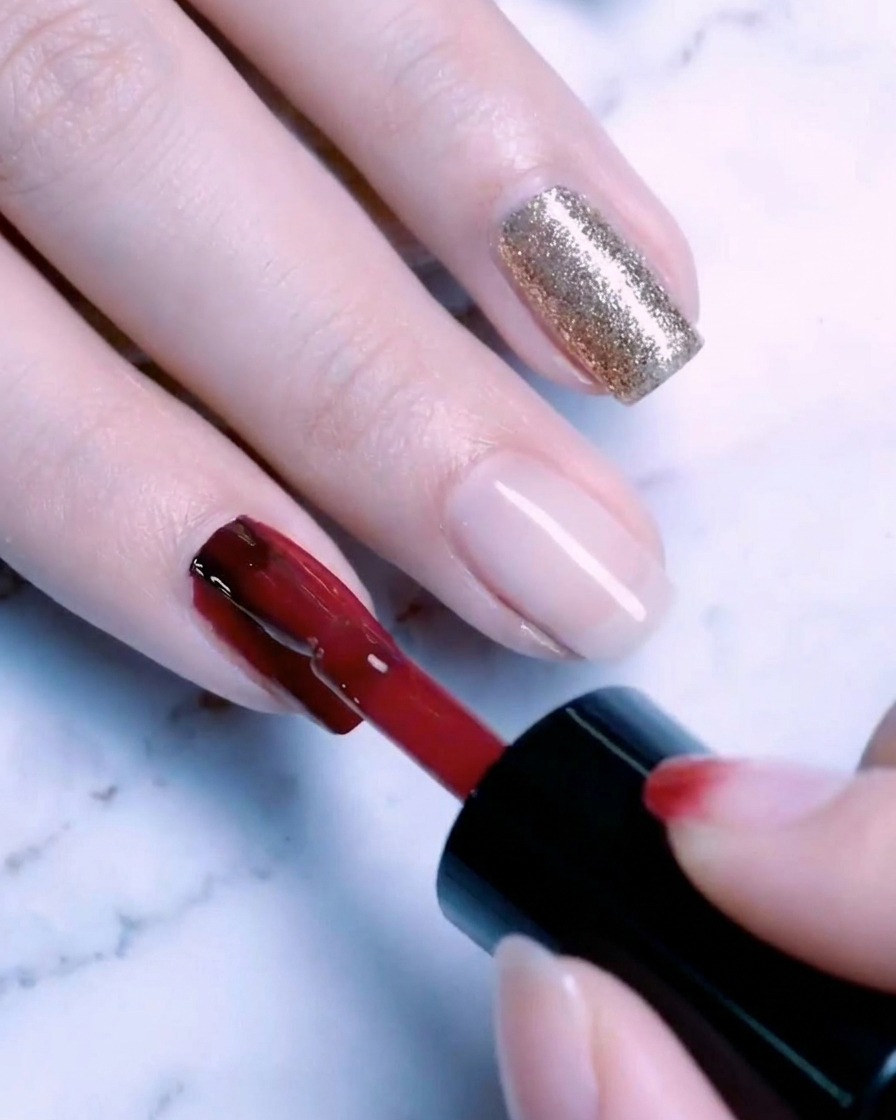A brush applying a second coat of gold glitter gel to the nail, creating a rich, sparkling finish.