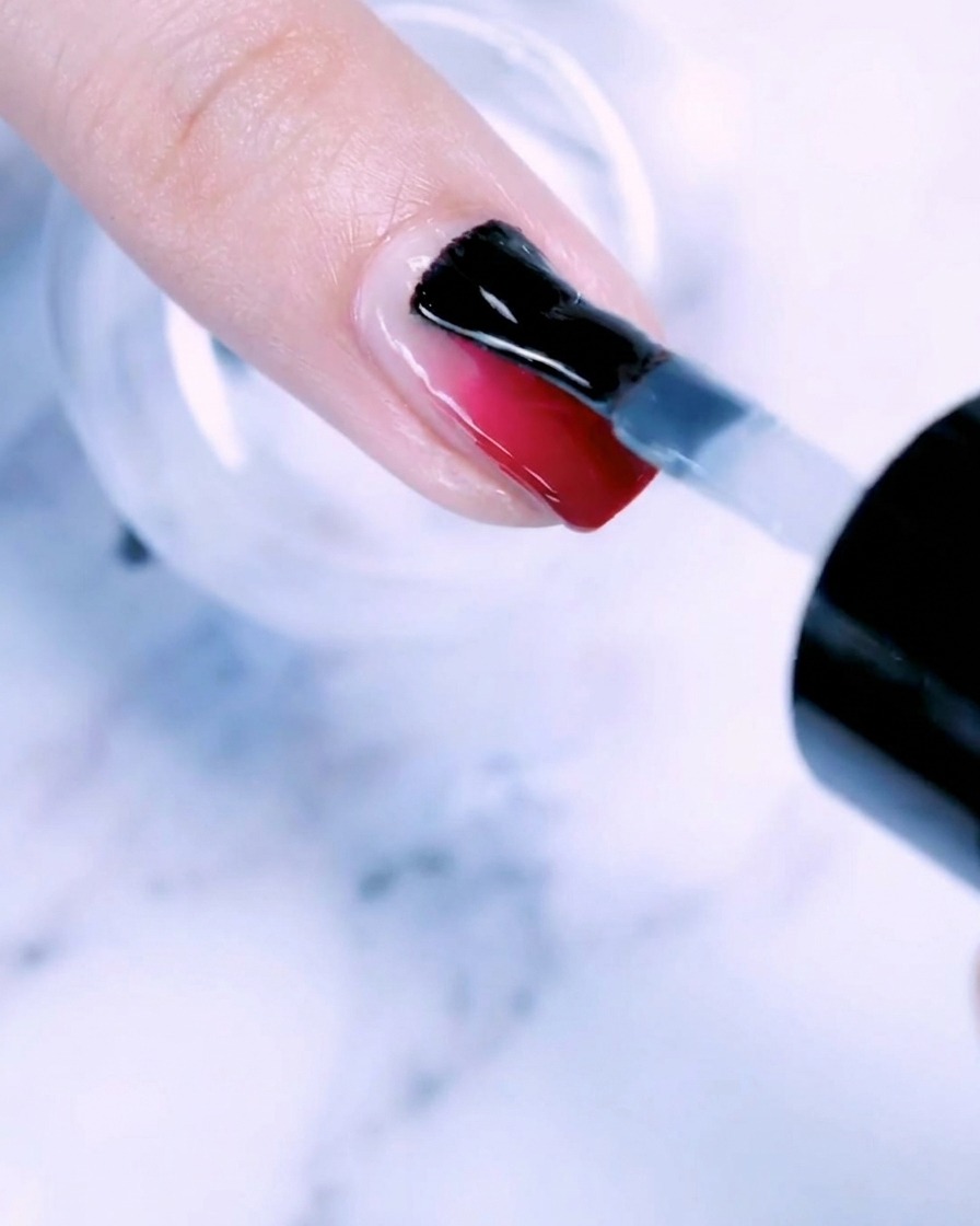 A brush applying a clear coat of base gel to a fingernail with a rose gold gradient.
