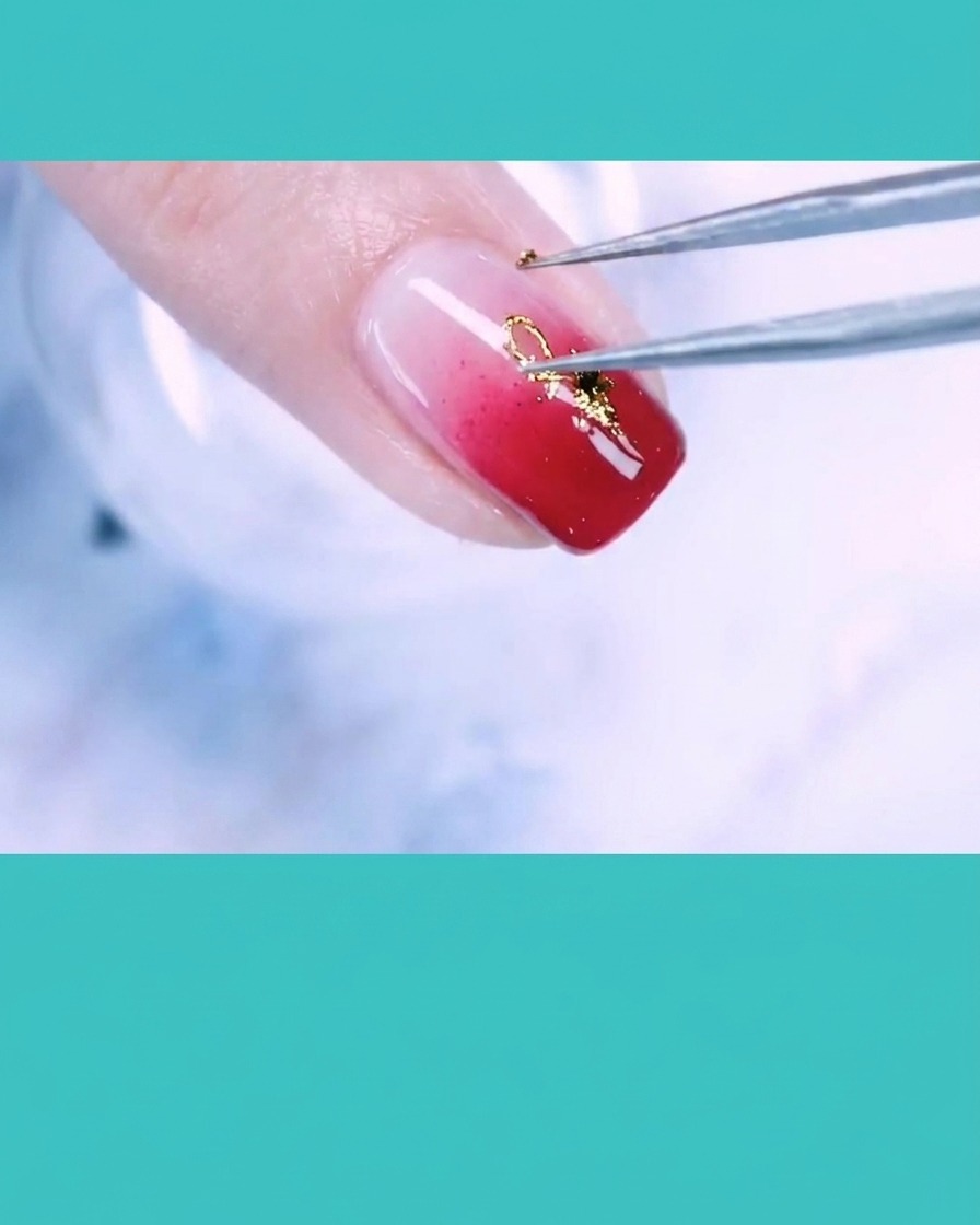 Tweezers placing a small gold wire accent onto a fingernail decorated with gold foil and pearls.